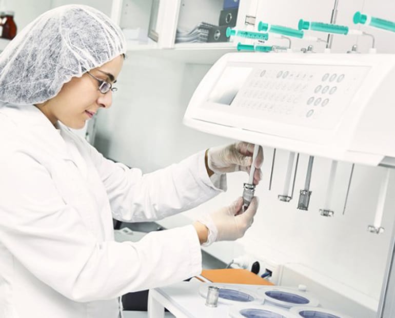Researcher in white lab coat and hair net works with samples in lab 