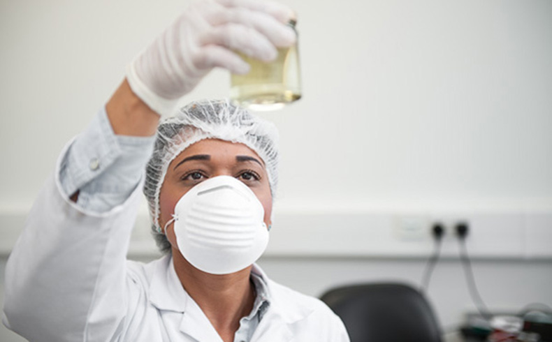 Lab Technician, wearing a face mask holding a glass beaker in the air