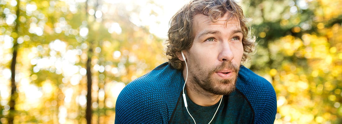 Male runner with white earphones exhales on a run 