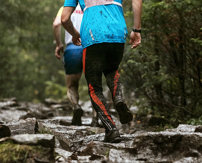 Two athletes run through mud and stones