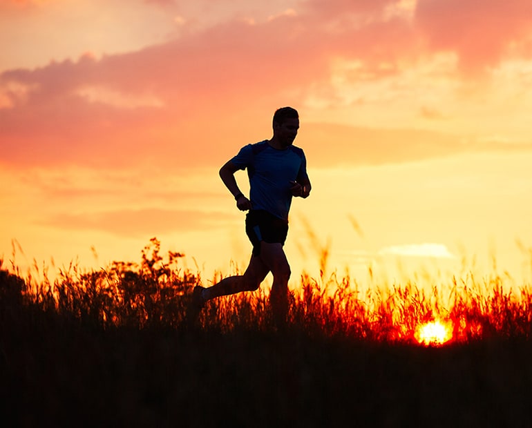 Male running across country at sunset 