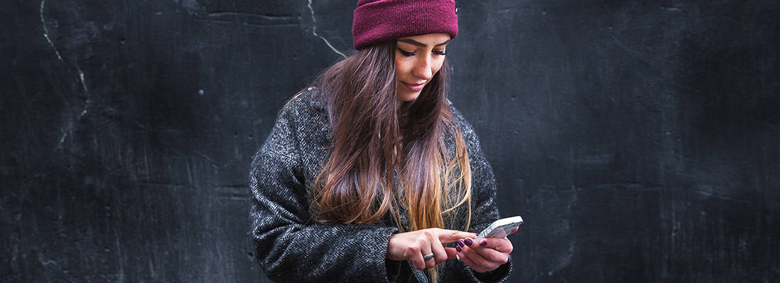 Female in coat and beanie hat scrolling on her phone