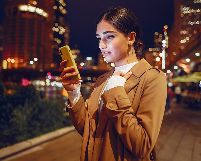 Female scrolling on her phone on a city street at night