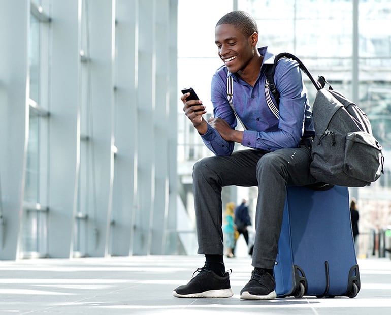 Male with. blue shirt and backpack sitting on a suitcase
