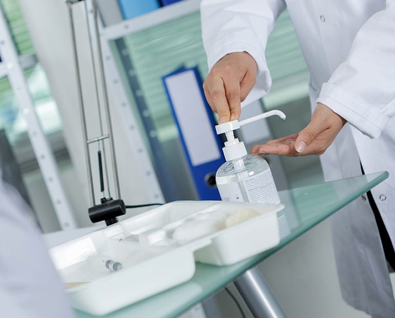 Male in white lab coat using hand sanitiser 