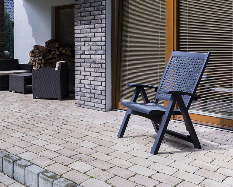 Black plastic garden chair sitting on a patio with large windows behind 