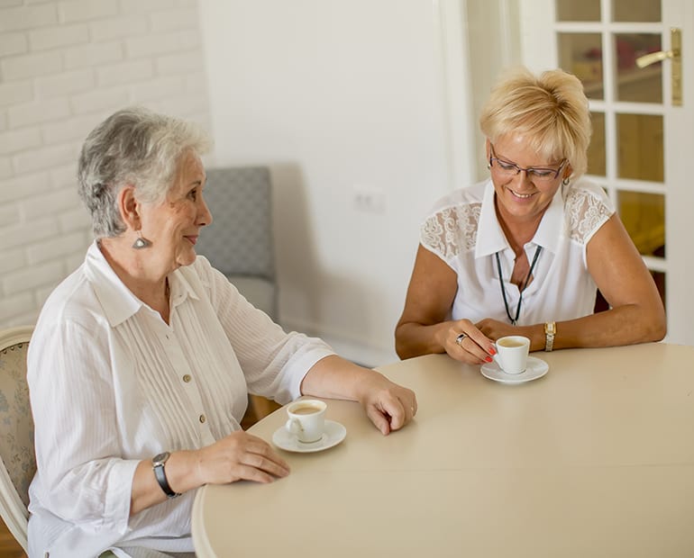 Two females drinking coffee at a round table 