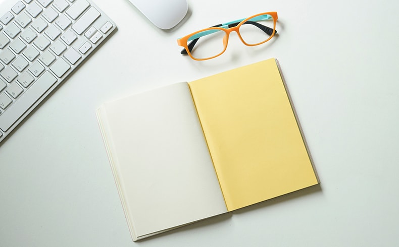 Close up of a pair of reading glasses and a blank notebook sitting on a computer desk
