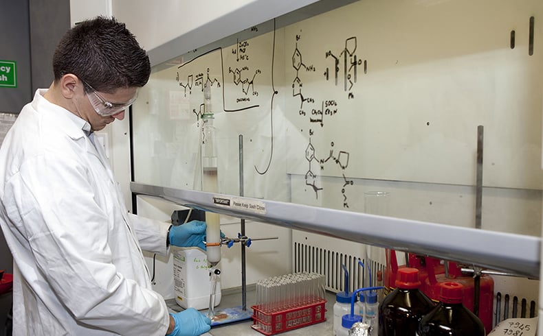 Researcher wearing white lab coat and goggles working in CREST lab