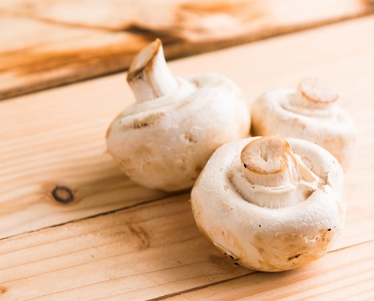 Three white mushrooms sitting on a wooden board
