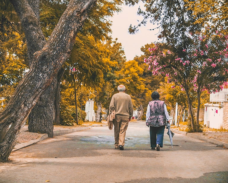 Elderly couple walking on a path with trees on both sides
