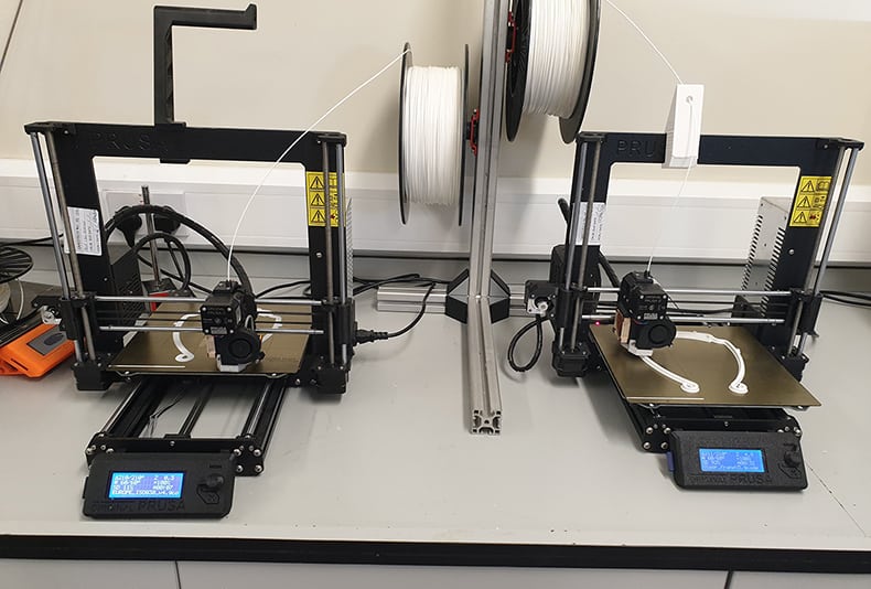 Two 3D printers side by side printing face shields