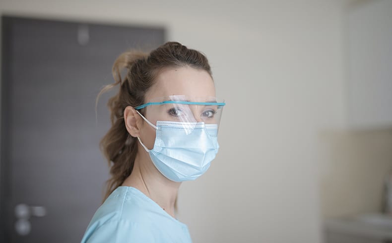 Female in blue shirt facing camera wearing a medical mask and face visor
