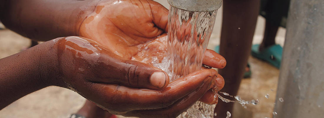 Hands gathering water under a water pump