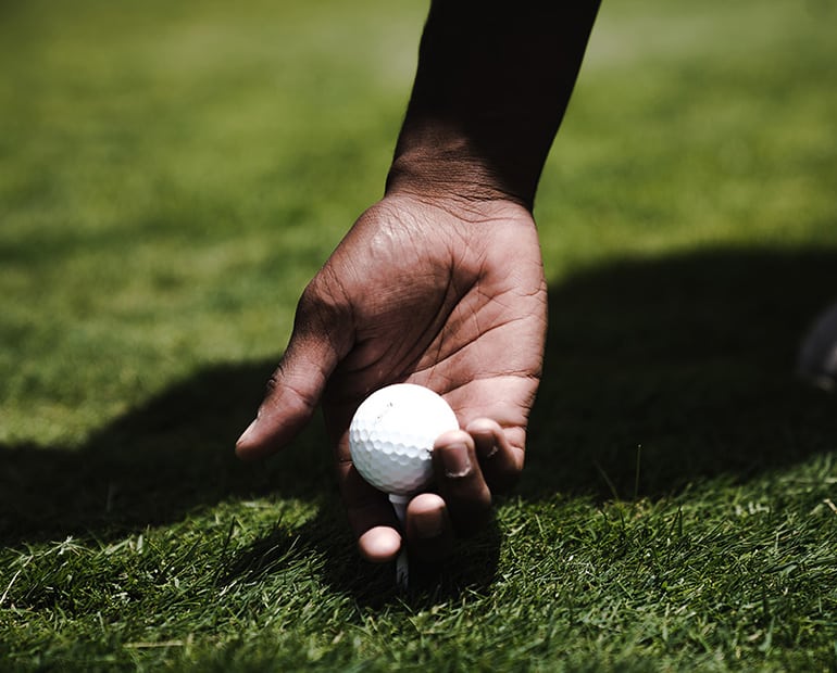 Close up of hand placing golf ball and tee into ground 