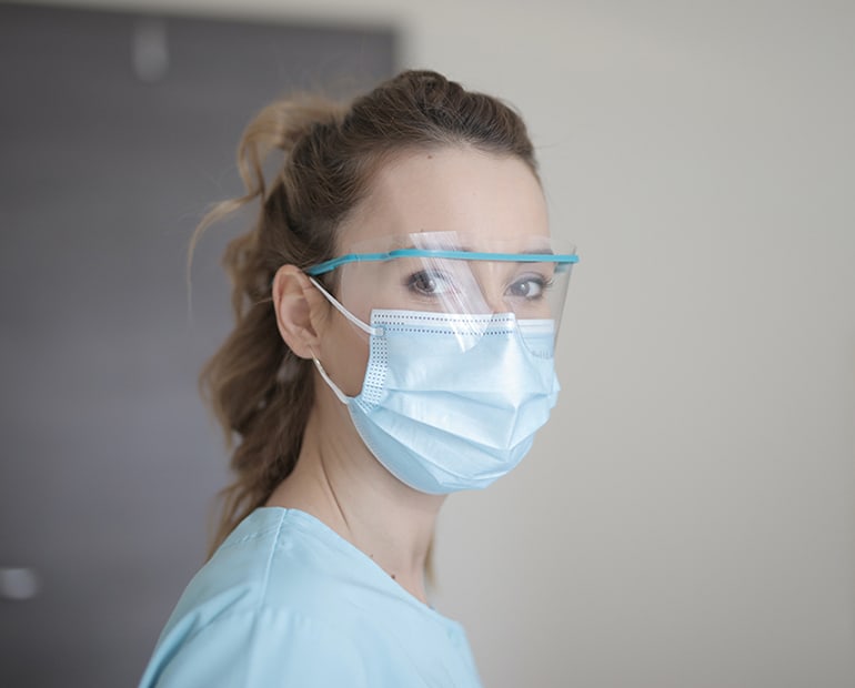 female doctor in scrubs with medical face mask and visor 