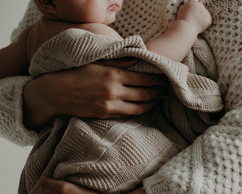 Baby held by parent in cream knitted blanket