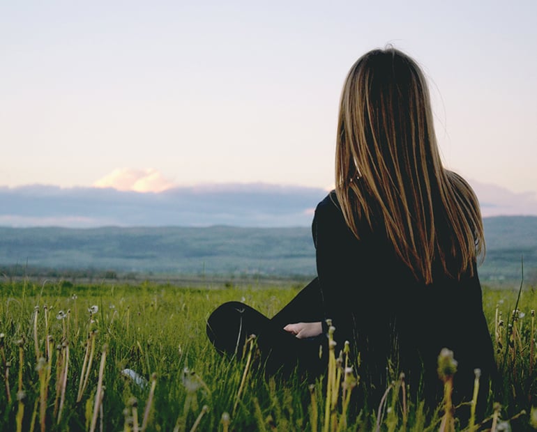 Female sitting on green looking at mountain view 