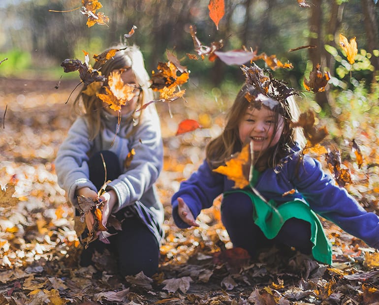 Two young girls playing with autumn leaves