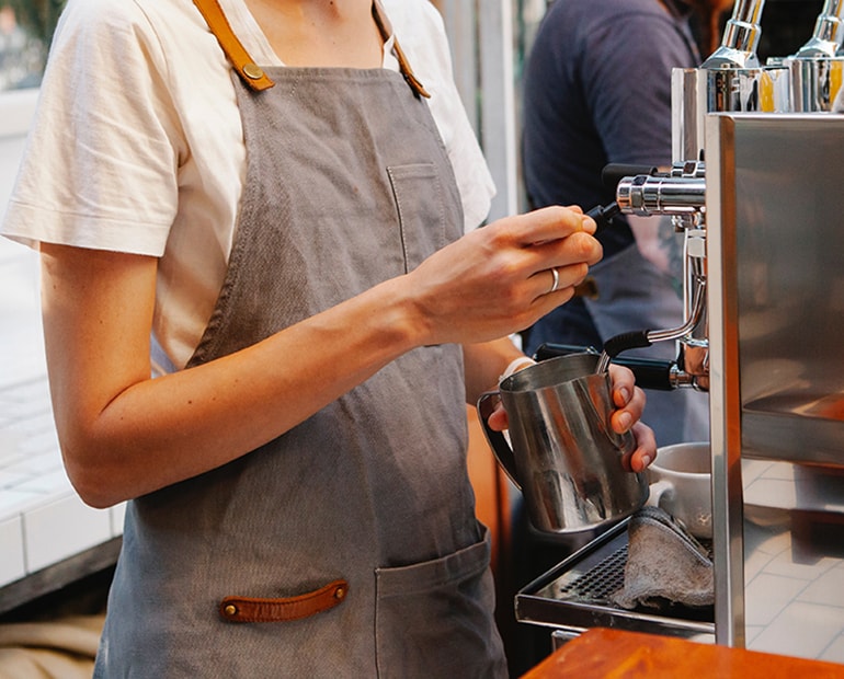Female with apron making coffee at a coffee machine