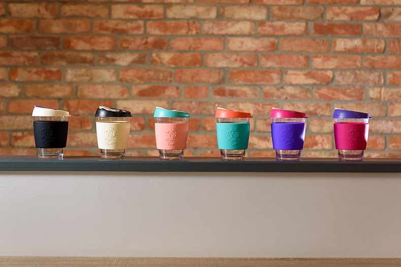 Six colourful Monkeycups in a row with a brick wall behind