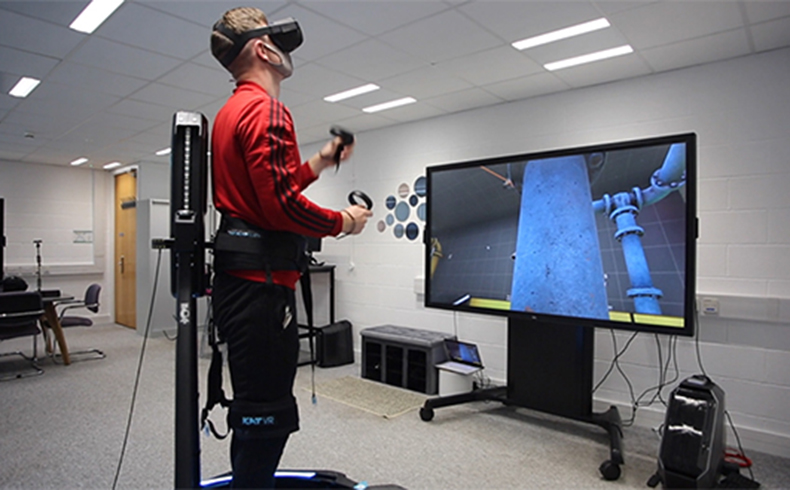 Male researcher wearing a VR headset and holding controllers standing in front of a large screen