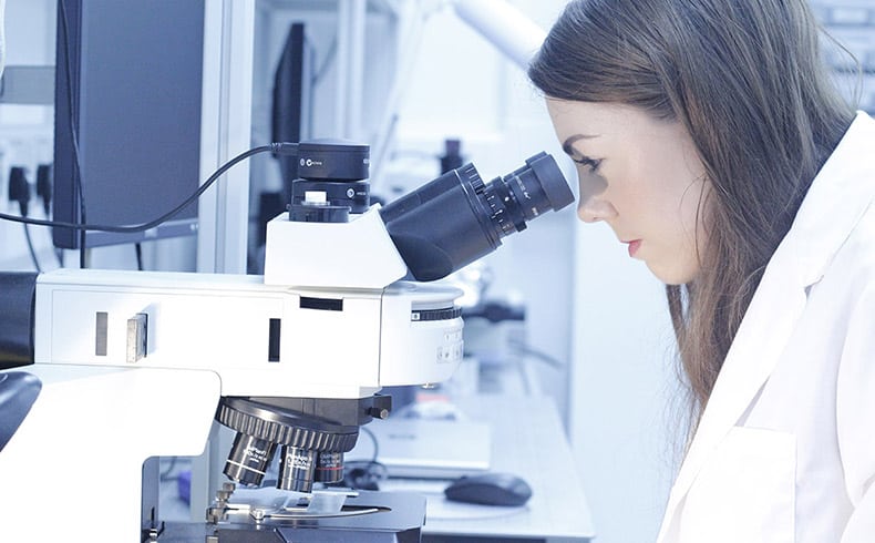 Female researcher in white lab coat looking into a microscope