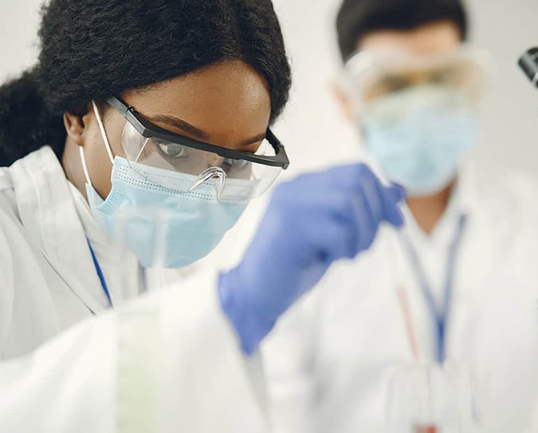 Female researcher in white lab coat, safety goggles and face mask