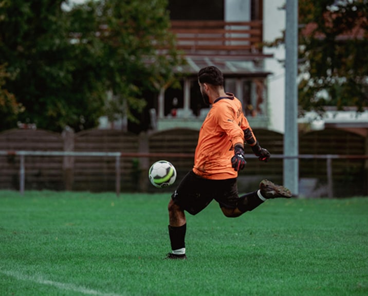 Soccer Player in Orange T-Shirt Kicking a Ball
