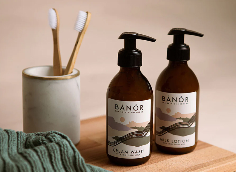 2 brown bottle Banor products sitting on wooden shelf with a green face cloth and two tooth brushes in a ceramic container