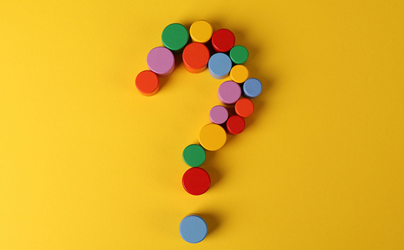 Colourful wooden shapes forming a question mark on a yellow background