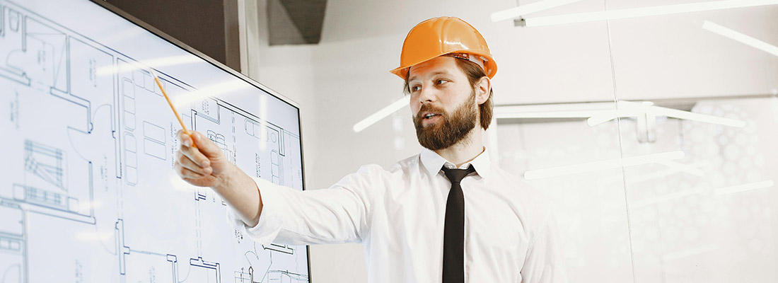 Man in orange hard hat pointing at a large screen showing construction drawings