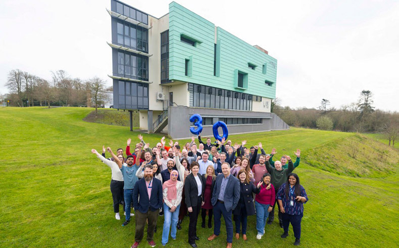 Group of people in front of Walton institute building with blue balloons in the numbers 3 and 0.